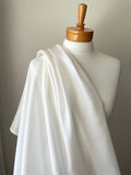 White silk mesh fabric draped over a mannequin with a wooden head on a neutral background