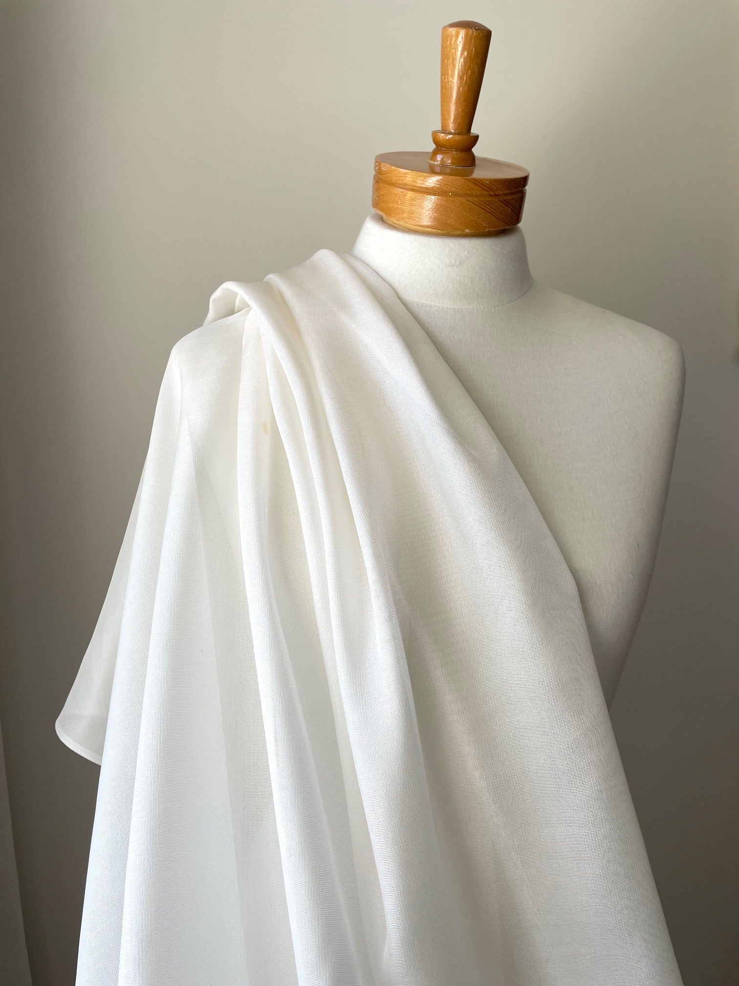 White silk mesh fabric draped over a mannequin with a wooden head on a neutral background