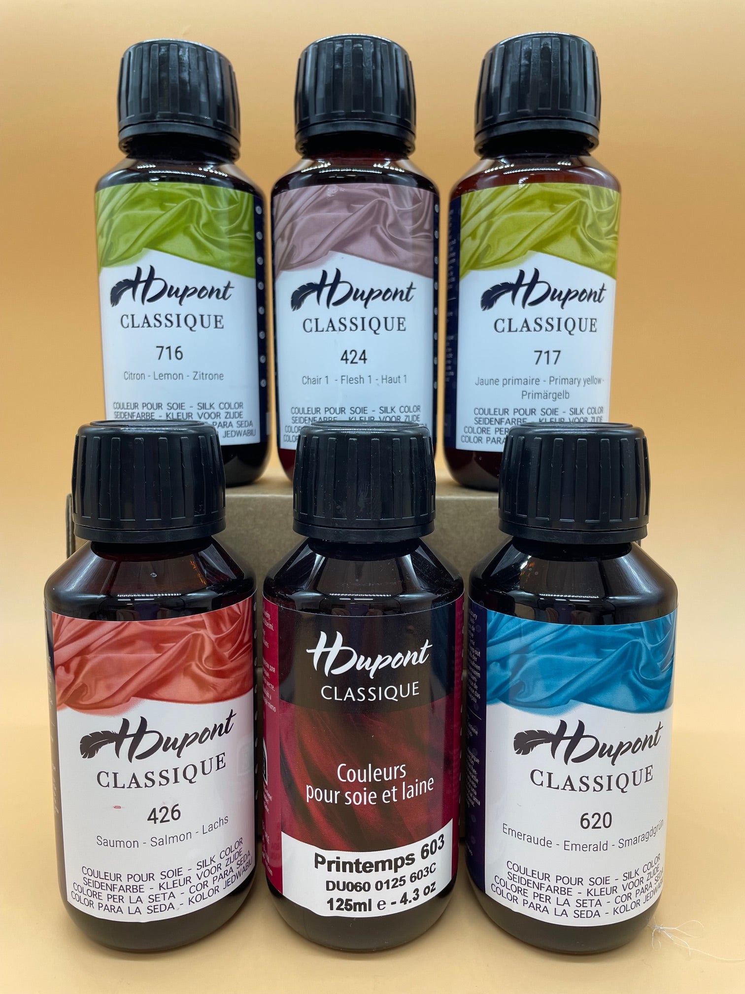 Collection of H Dupont silk dye bottles with colorful labels on a beige background