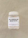 Small plastic container labeled 'Aluminium Acetate' on a beige background
