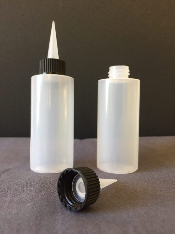Two plastic applicator bottles with black caps on a gray surface and dark background