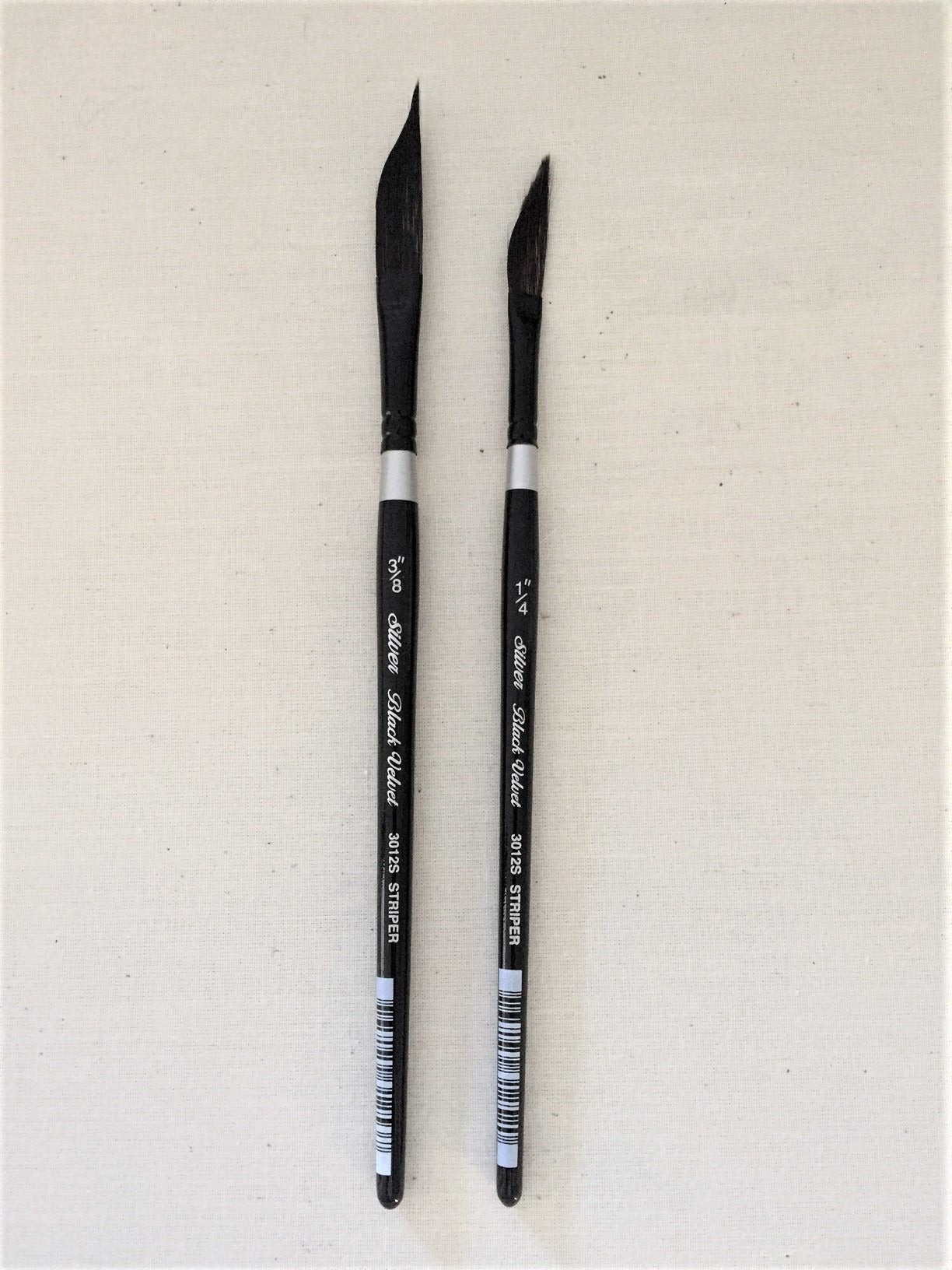 Two black paintbrushes with silver ferrules on a beige background