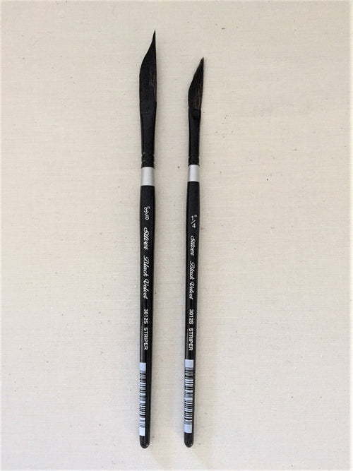 Two black paintbrushes with silver ferrules on a beige background