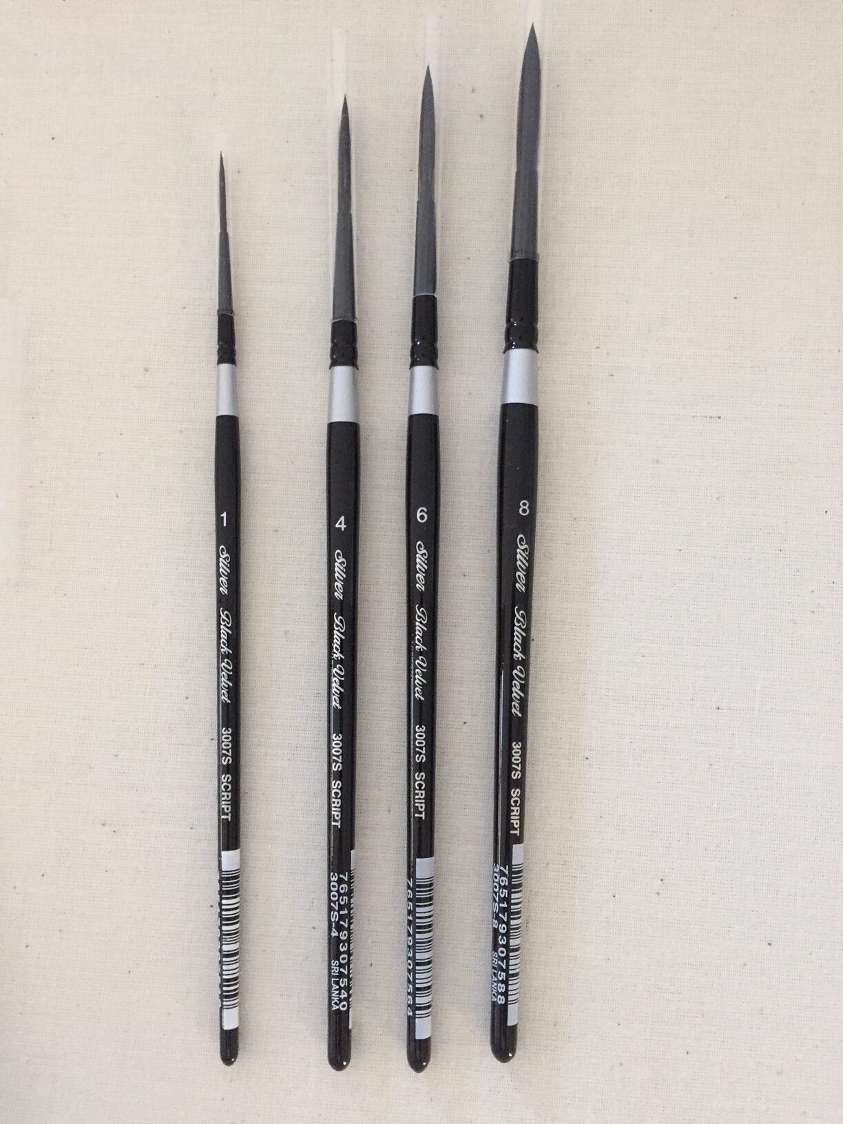 Four script liner paintbrushes of different sizes on a light gray background