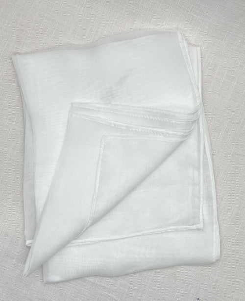 A folded white chiffon scarf with a stitched border, displayed on a textured beige linen surface.