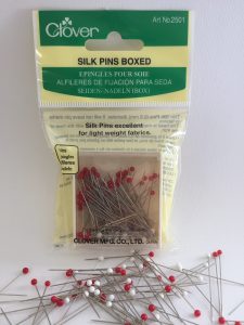 Package of Clover silk pins with pins scattered on a white background