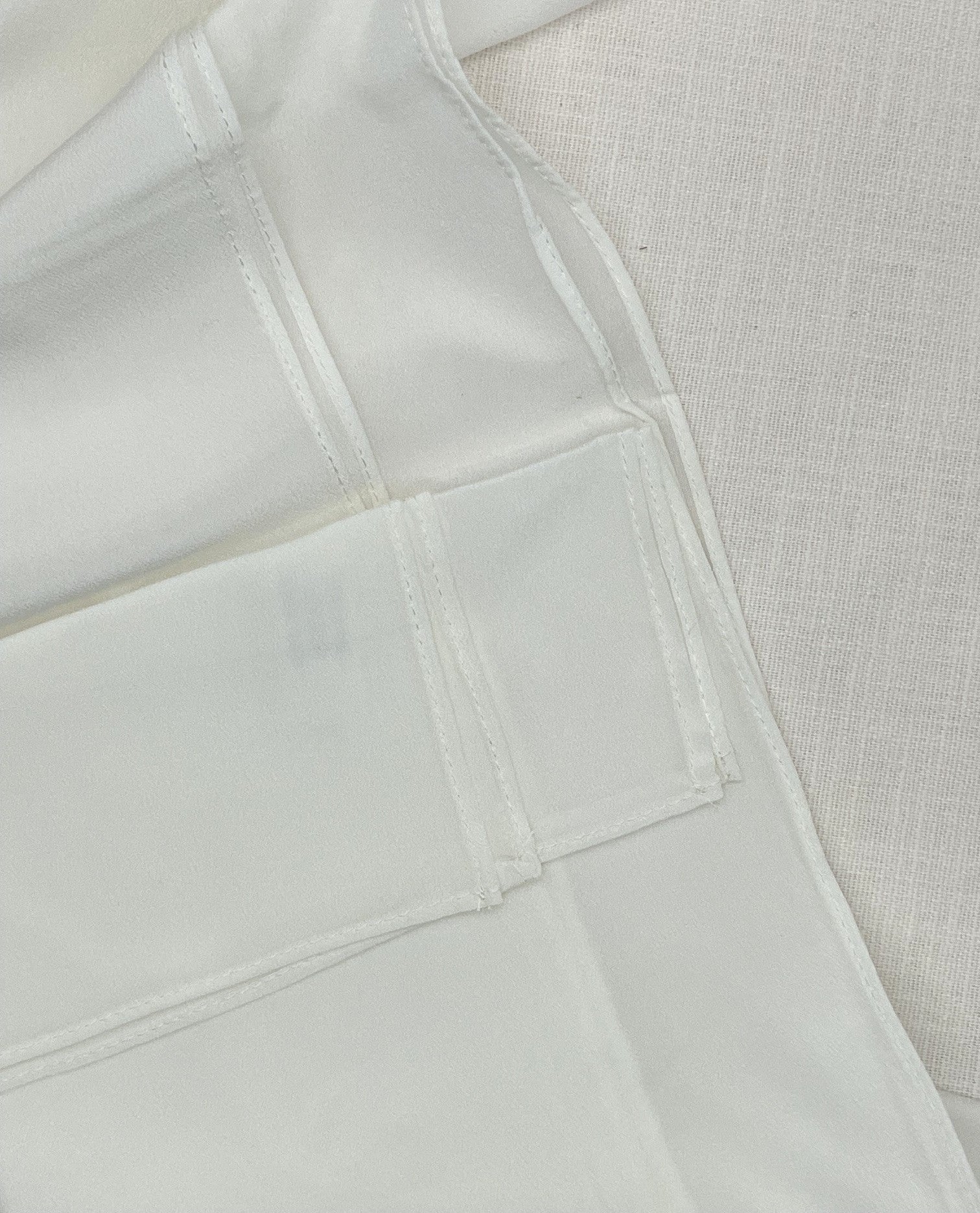 Close-up of a undyed machine hem scarf with visible seams and a textured off-white woven fabric background.