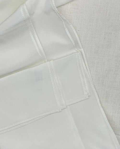 Close-up of a undyed machine hem scarf with visible seams and a textured off-white woven fabric background.