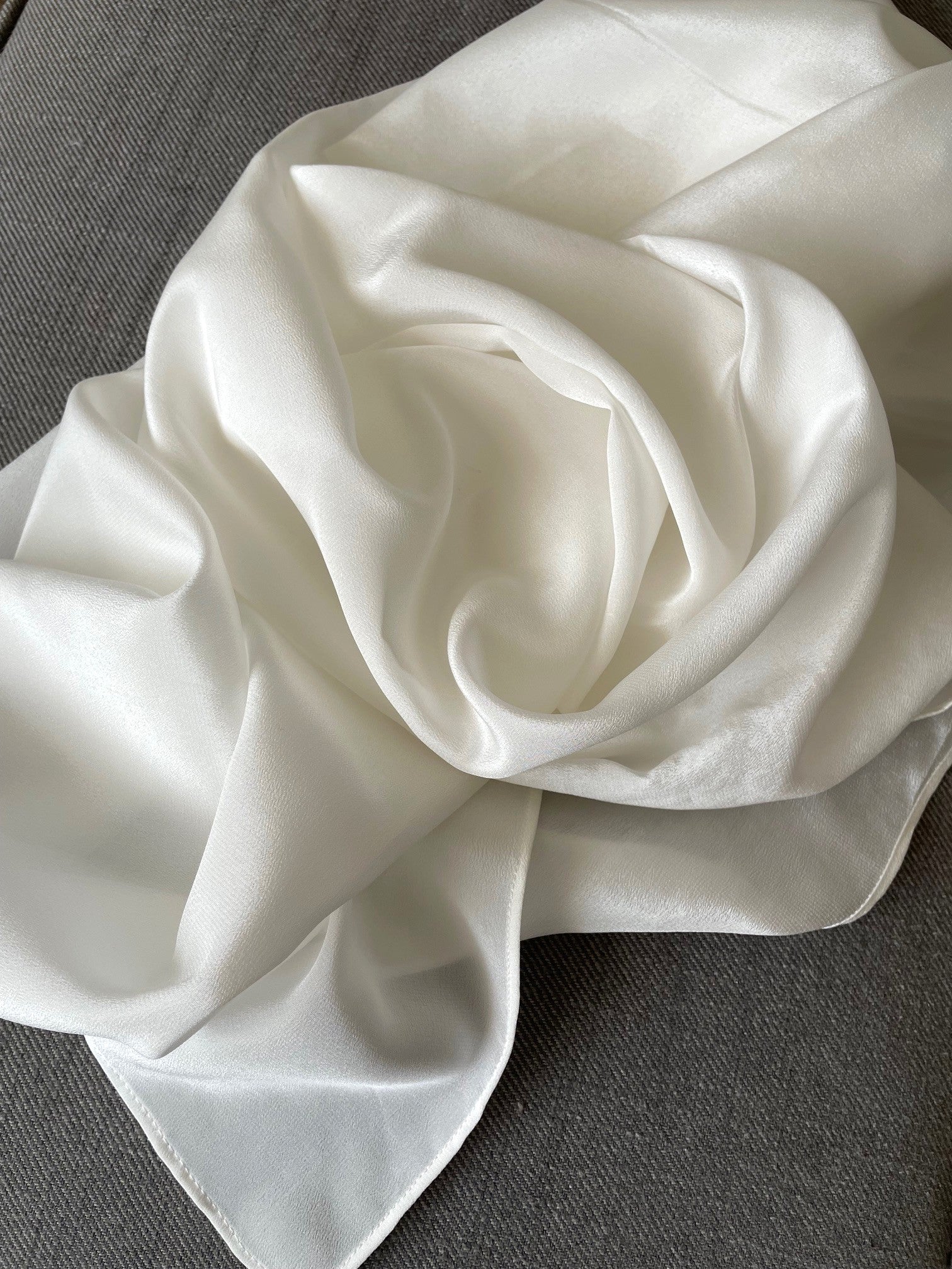 Crumpled undyed white crepe de chine scarf on a gray surface