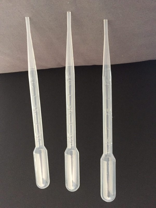 Three clear plastic pipettes on a dark surface with a gray background