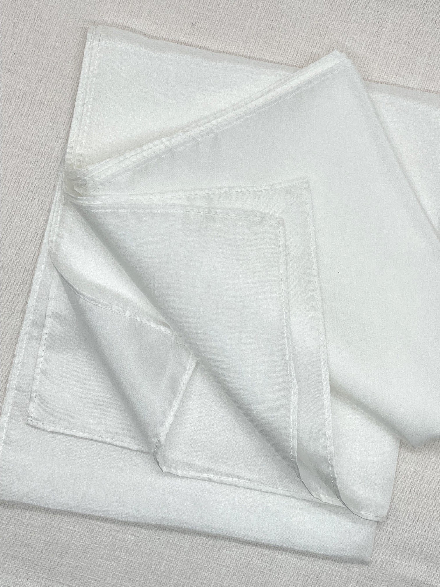 Undyed Habutai silk scarf showing machine hems on a beige linen background