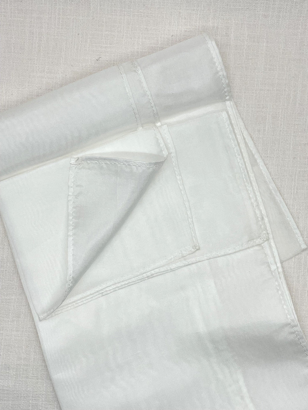 Undyed Paj silk scarf folded showing machine hems on a linen backgound