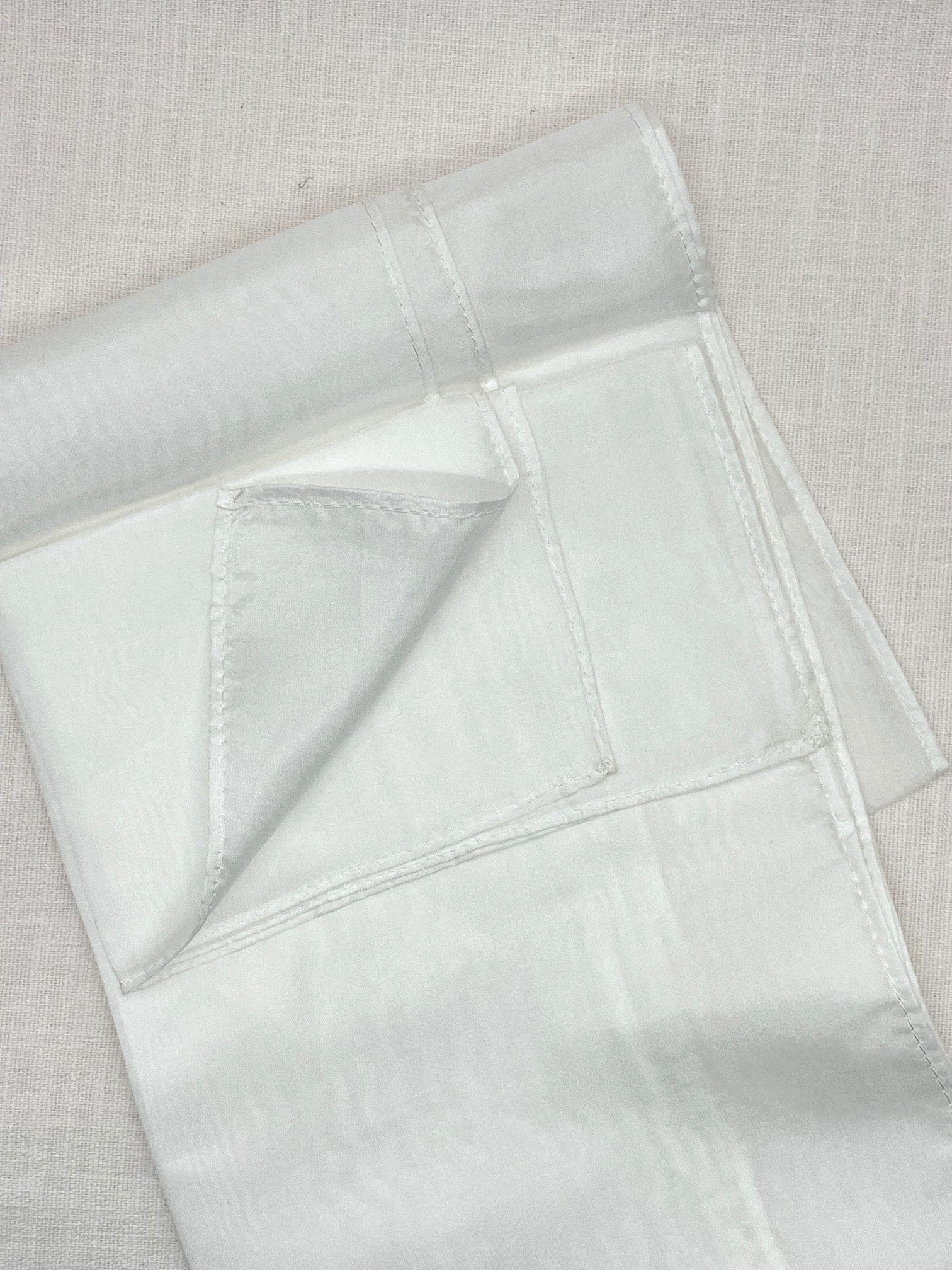 Undyed Paj silk scarf folded showing machine hems on a linen backgound