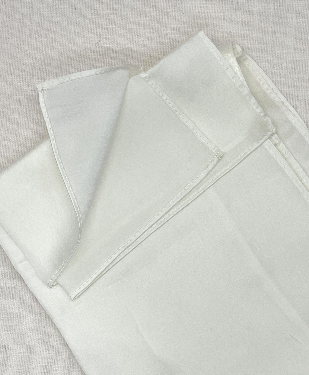 Silk satin crepe machine hemmed scarf folded on a beige background