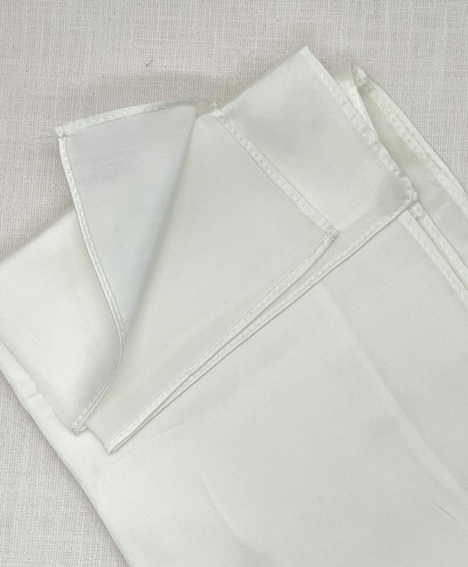 Silk satin crepe machine hemmed scarf folded on a beige background