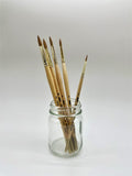Set of paintbrushes in a clear glass jar on a white background