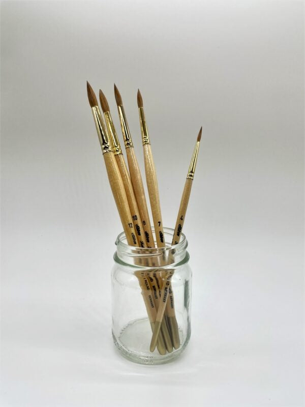 Set of paintbrushes in a clear glass jar on a white background