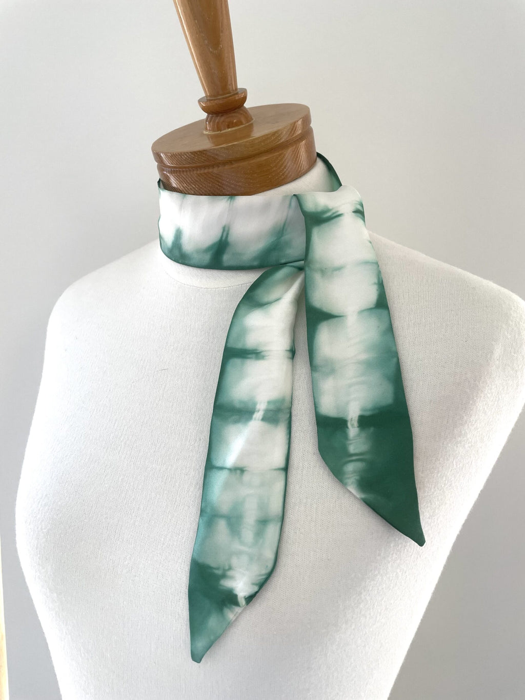 Green and white patterned scarf on a mannequin with a wooden stand against a white background