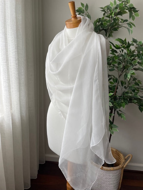 Undyed white scarf draped on a wooden hanger with a plant in the background
