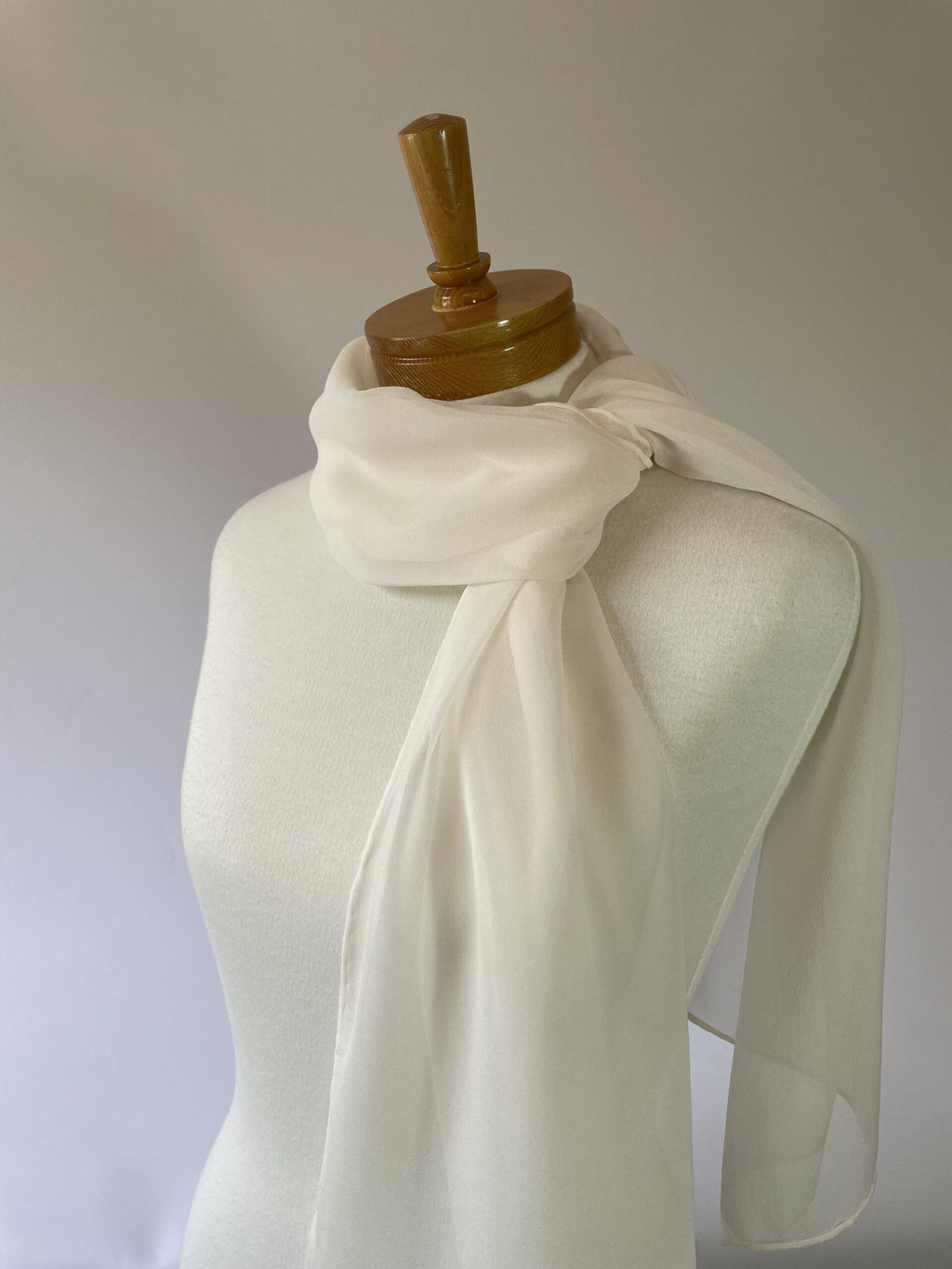 Undyed off white Georgette silk scarf draped over a mannequin with a wooden head on a plain background