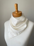 Close-up of an undyed white habutai bandana tied around the neck of a mannequin against a grey background