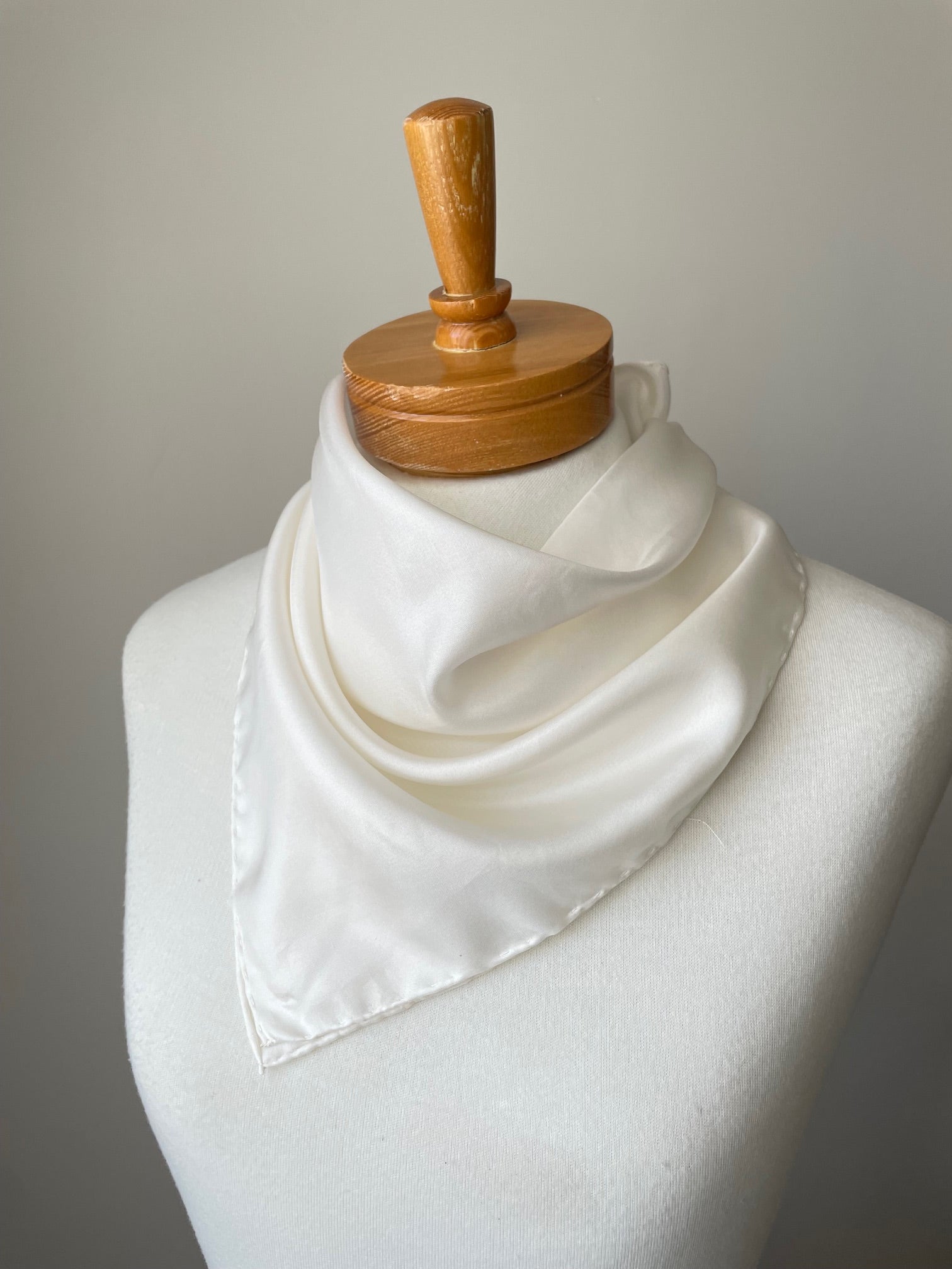 Close-up of an undyed white habutai bandana tied around the neck of a mannequin against a grey background