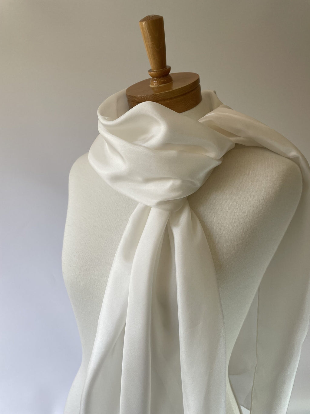 Undyed white habutai silk scarf draped over a mannequin with a wooden head on a plain background