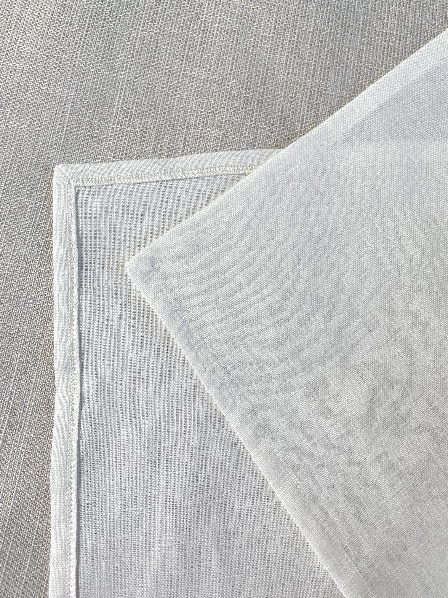 A close-up of a undyed woven linen panel folded over on a matching textured gray surface.