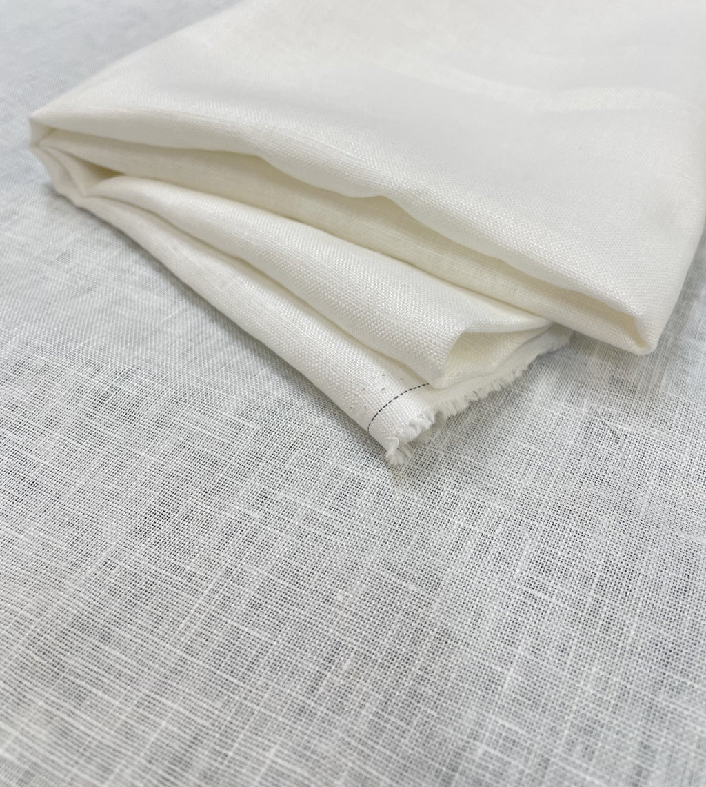 A folded piece of undyed heavy linen fabric with a textured weave, displayed on a light gray linen-like surface.