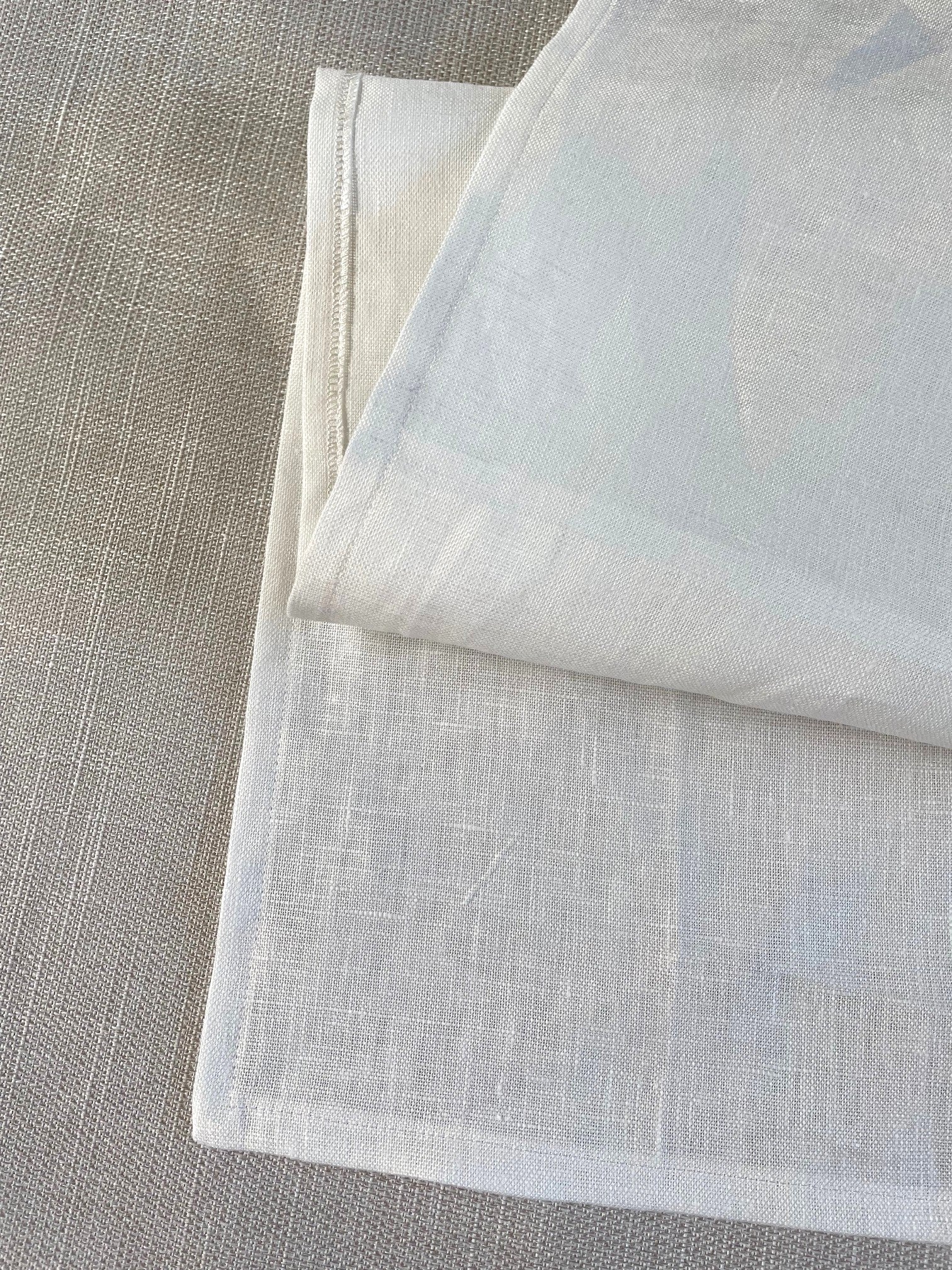 A folded undyed linen fabric napkin or table linen with a visible woven texture, displayed on a neutral gray linen surface.
