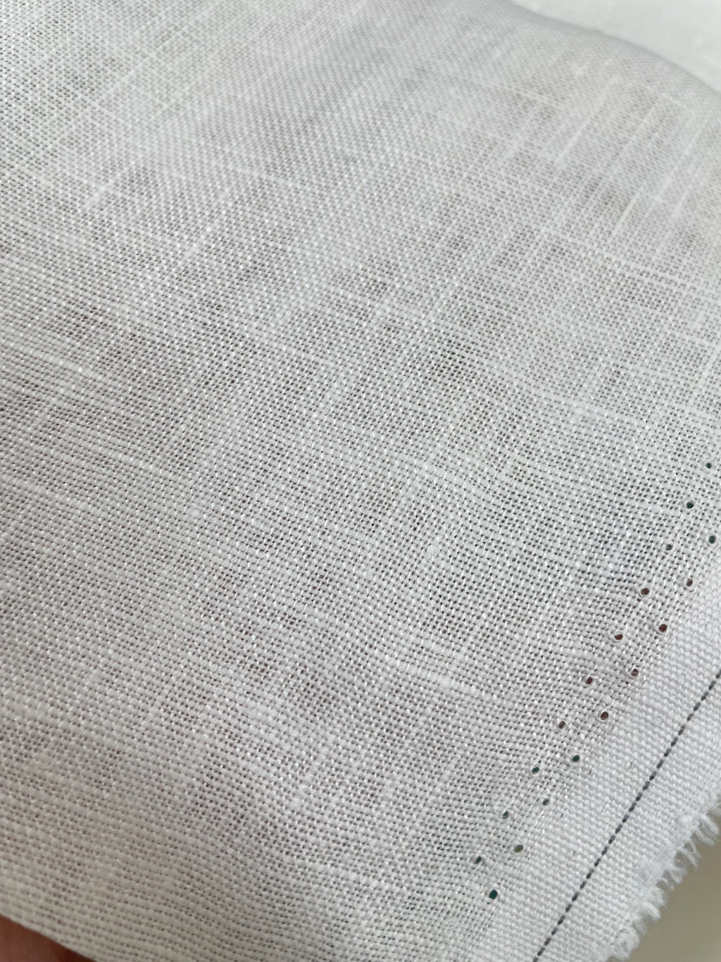 A close-up of a undyed heavy linen woven fabric with a visible texture and a stitched edge.