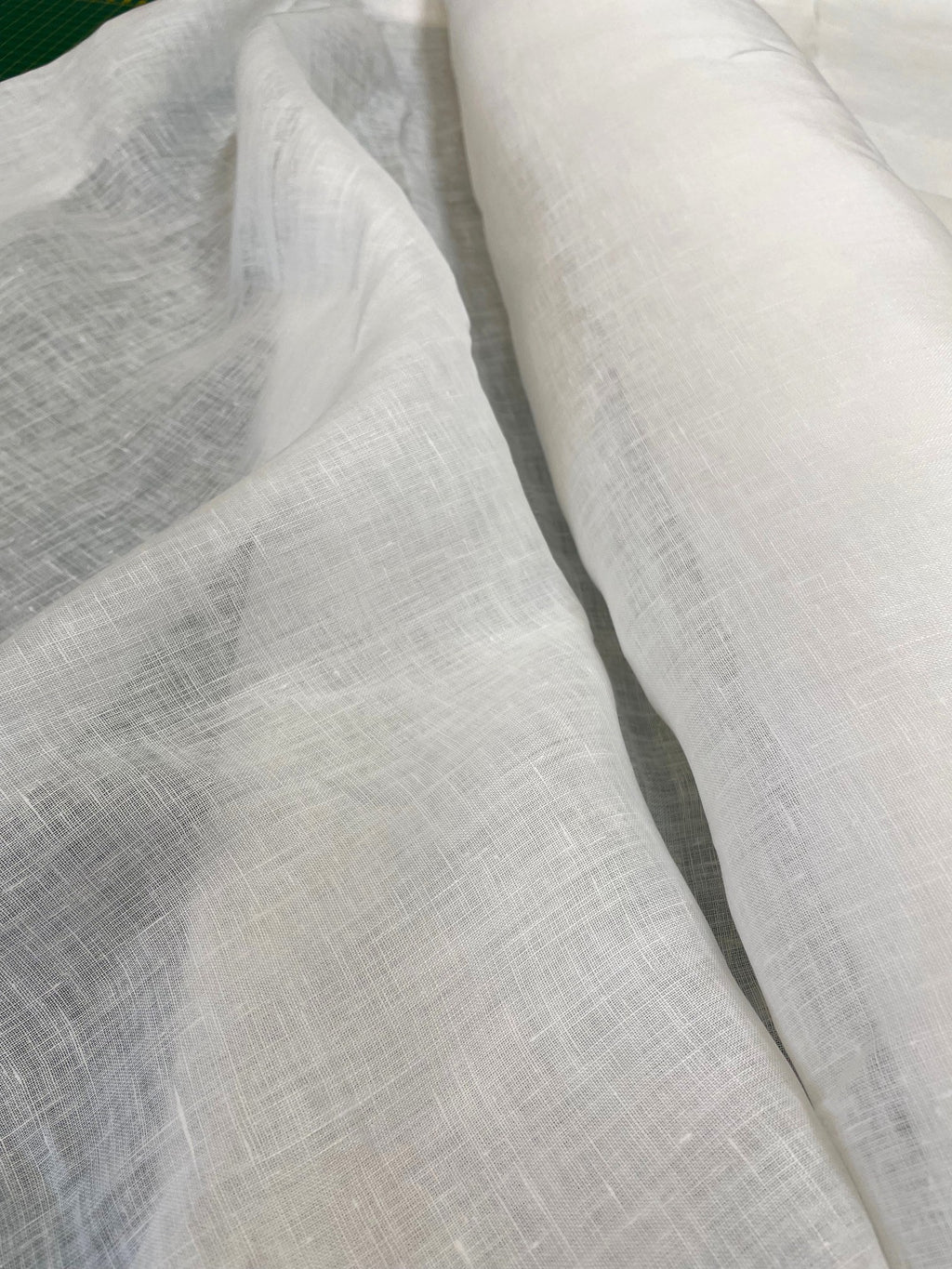A close-up of draped white linen fabric with a visible woven texture, showing soft folds and a rolled section of the same material.