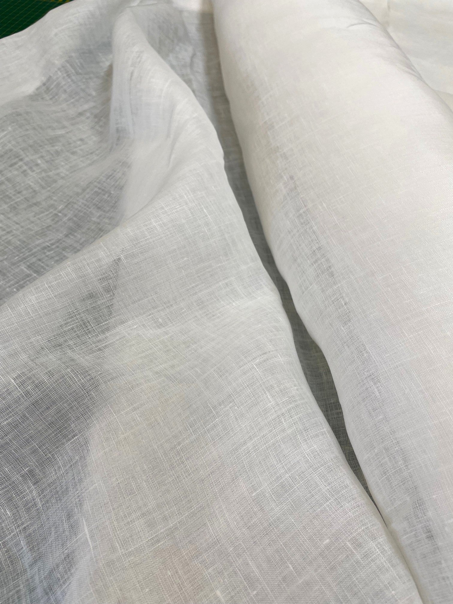 A close-up of draped white linen fabric with a visible woven texture, showing soft folds and a rolled section of the same material.
