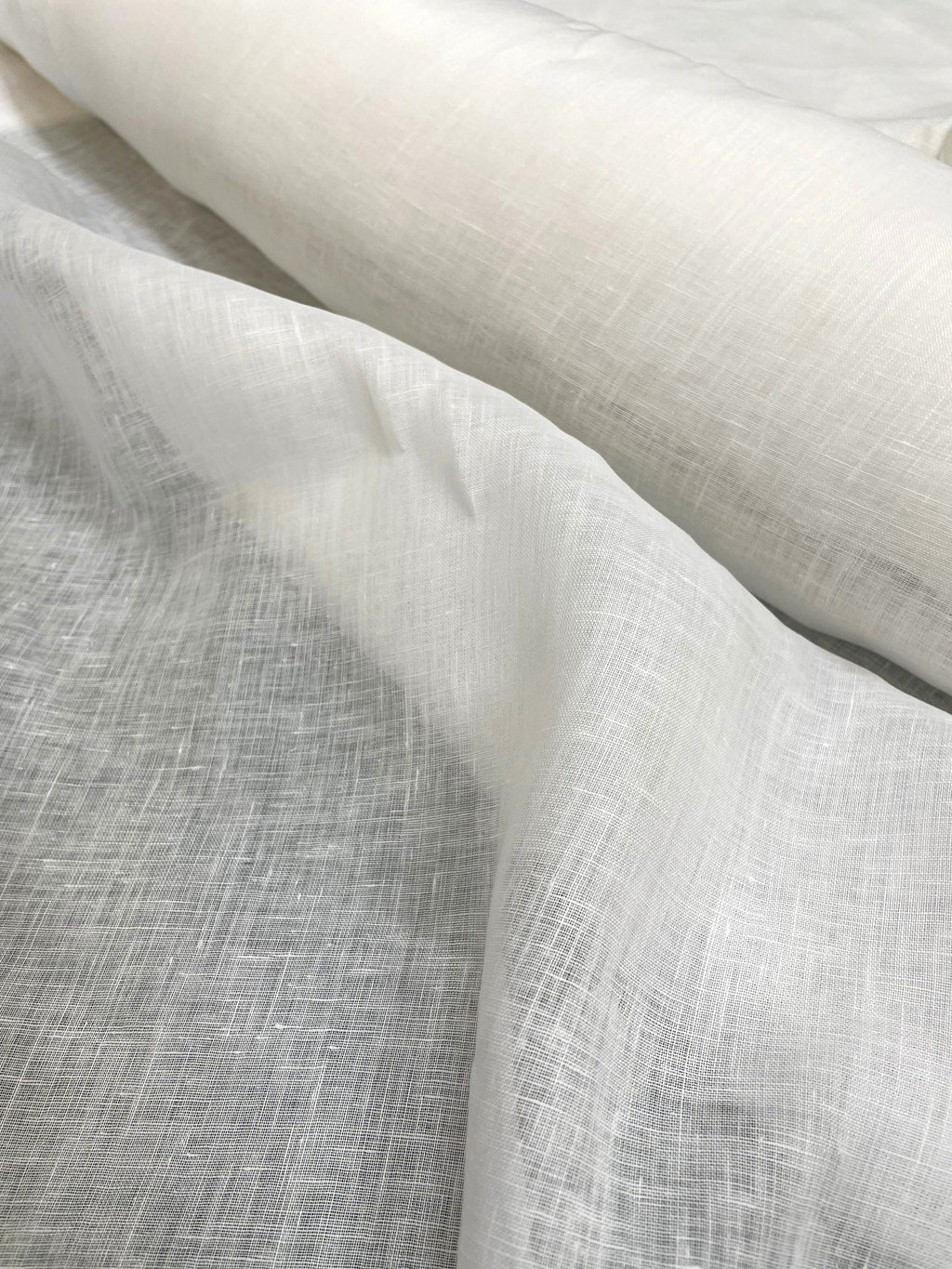 A close-up of draped undyed linen woven fabric with a visible linen-like texture, filling the frame.