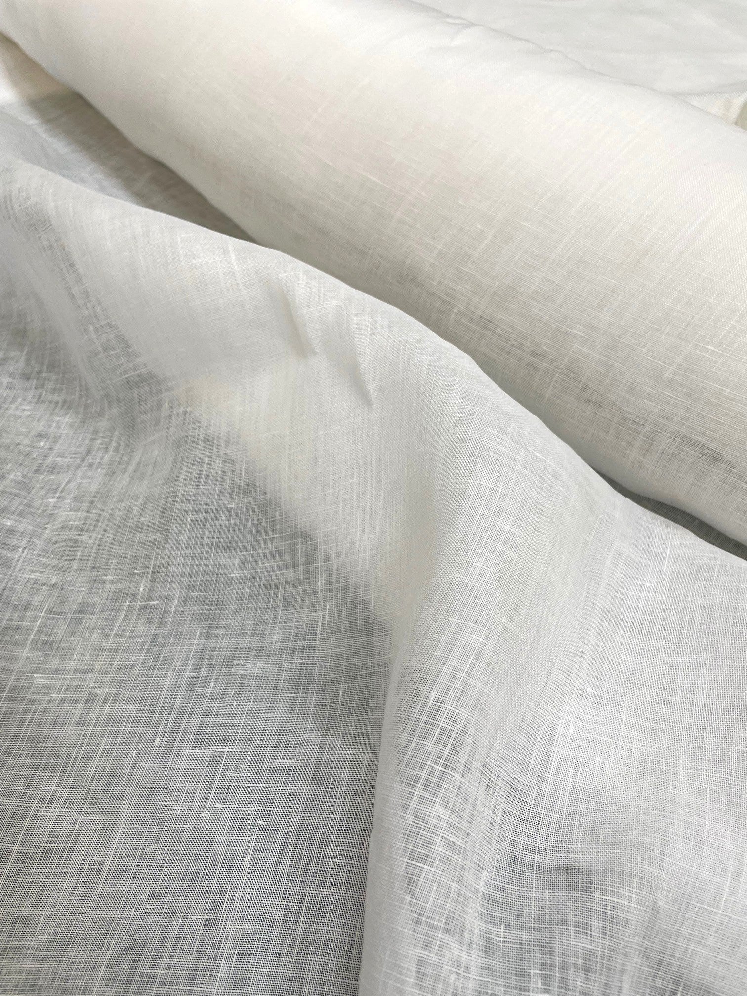 A close-up of draped undyed linen woven fabric with a visible linen-like texture, filling the frame.