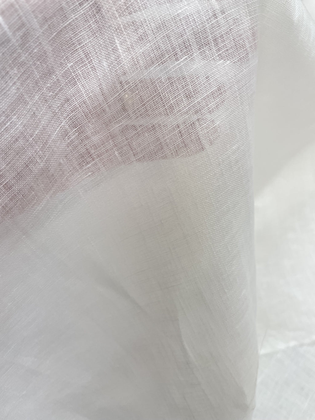 A close-up of sheer undyed linen fabric with a fine mesh texture, draped to show its lightweight quality and semi-transparency.