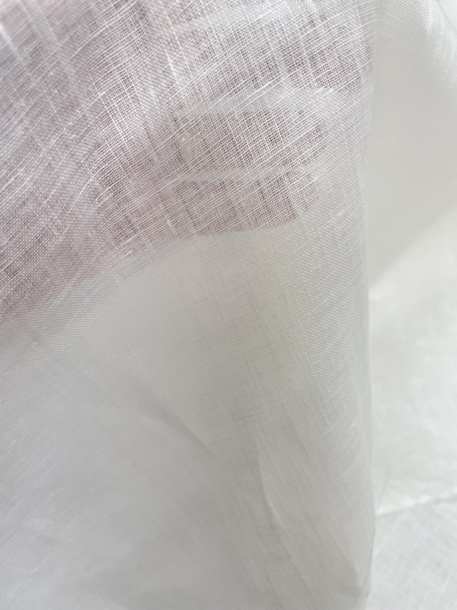 A close-up of sheer undyed linen fabric with a fine mesh texture, draped to show its lightweight quality and semi-transparency.