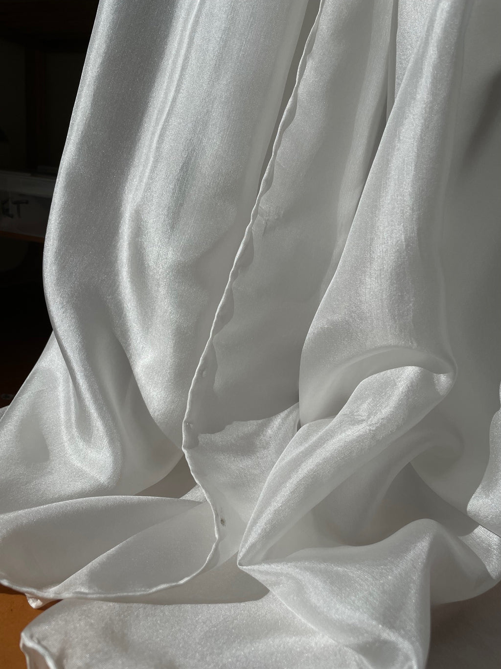 Close-up of undyed white Paj silk fabric with folds on a plain background