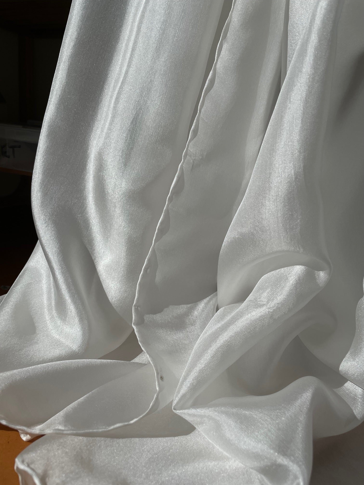 Close-up of undyed white Paj silk fabric with folds on a plain background