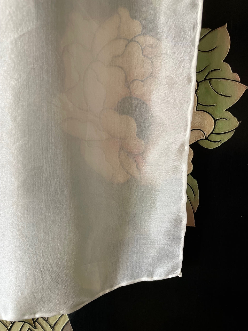 Undyed white Paj silk scarf with a floral design partially visible underneath, against a dark background.