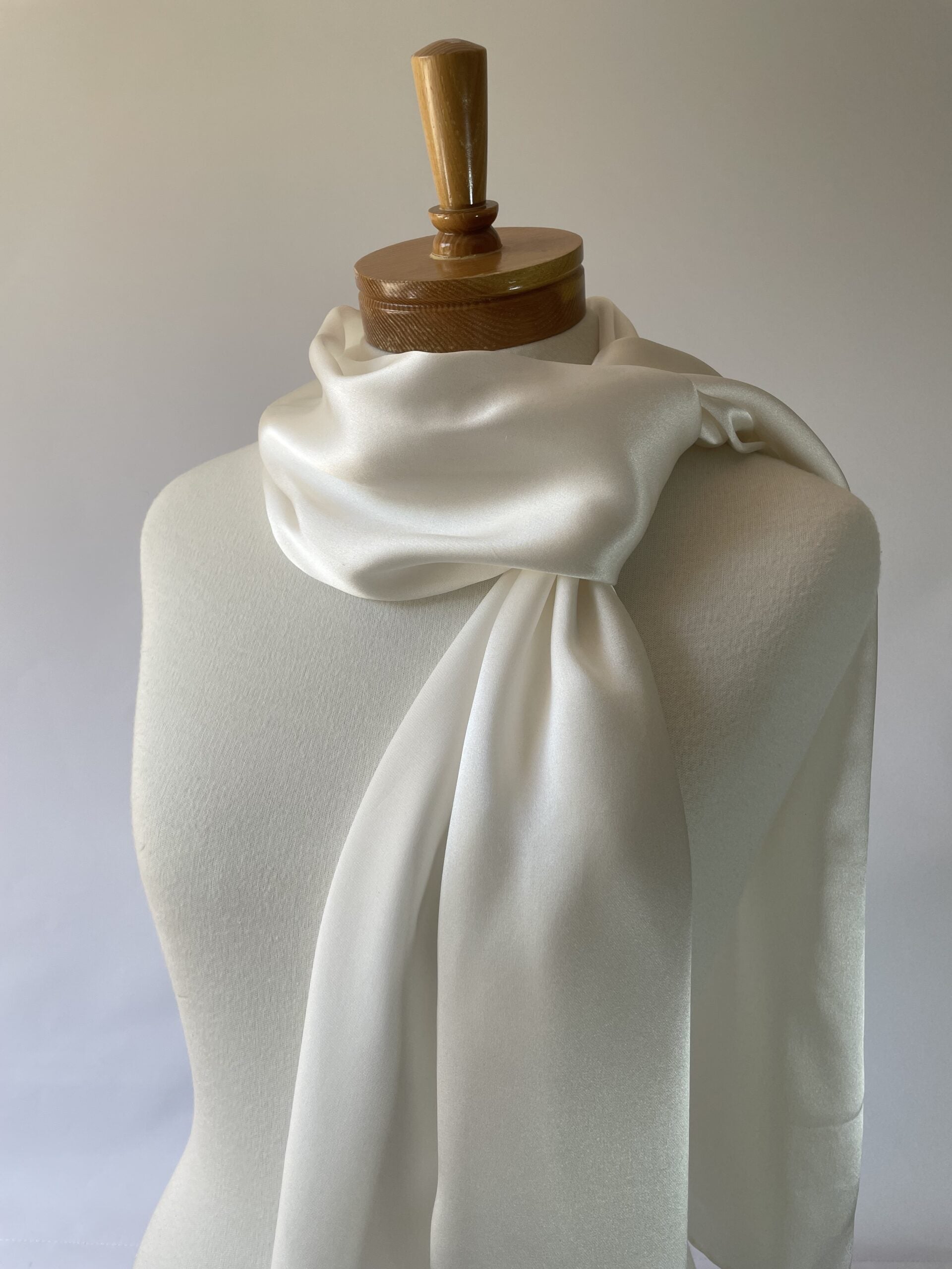 Undyed white silk satin crepe scarf draped over a mannequin with a wooden headrest against a plain background
