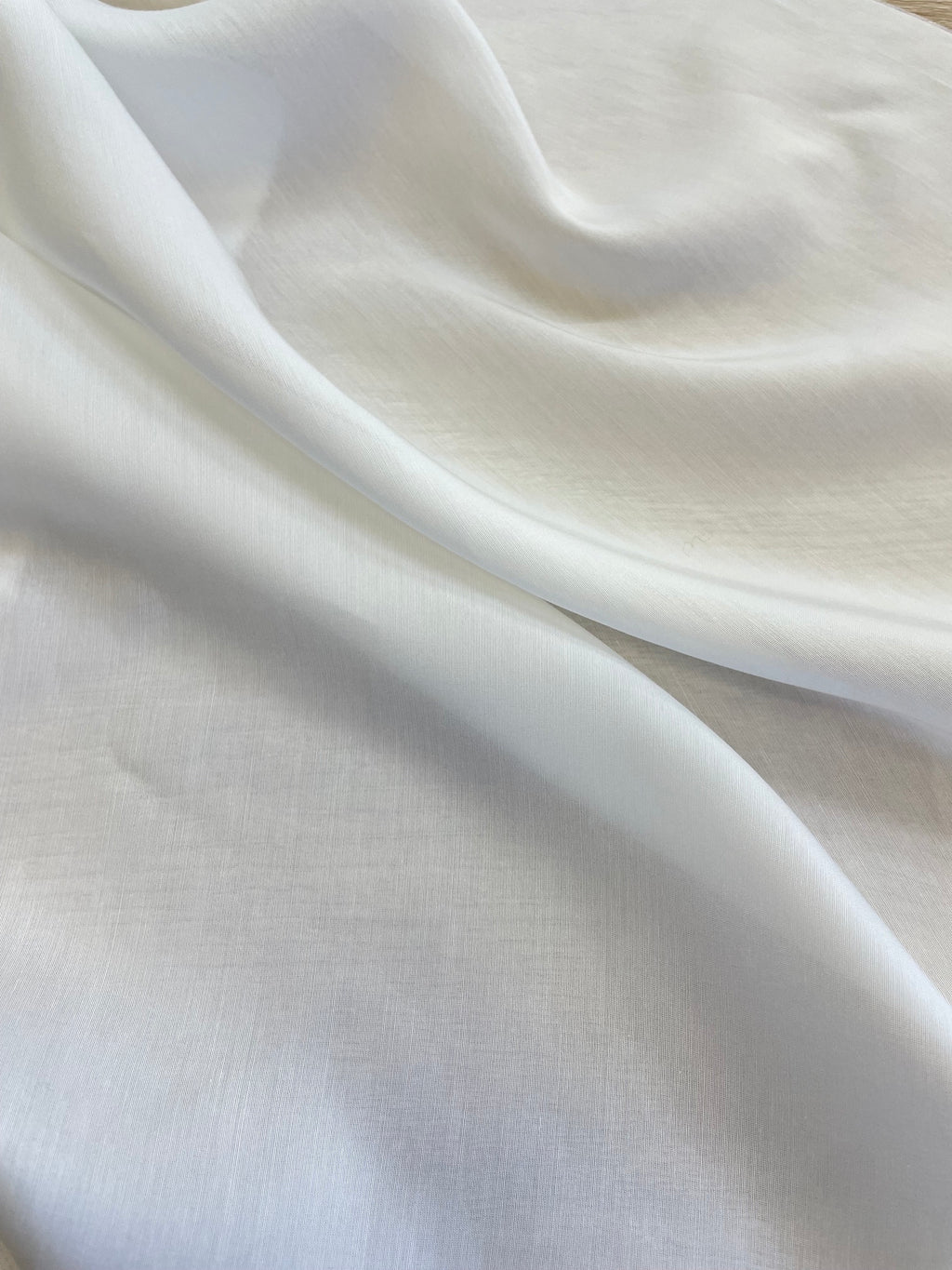 A close-up of draped undyed white silk bamboo fabric with soft folds and a smooth, slightly sheer texture.