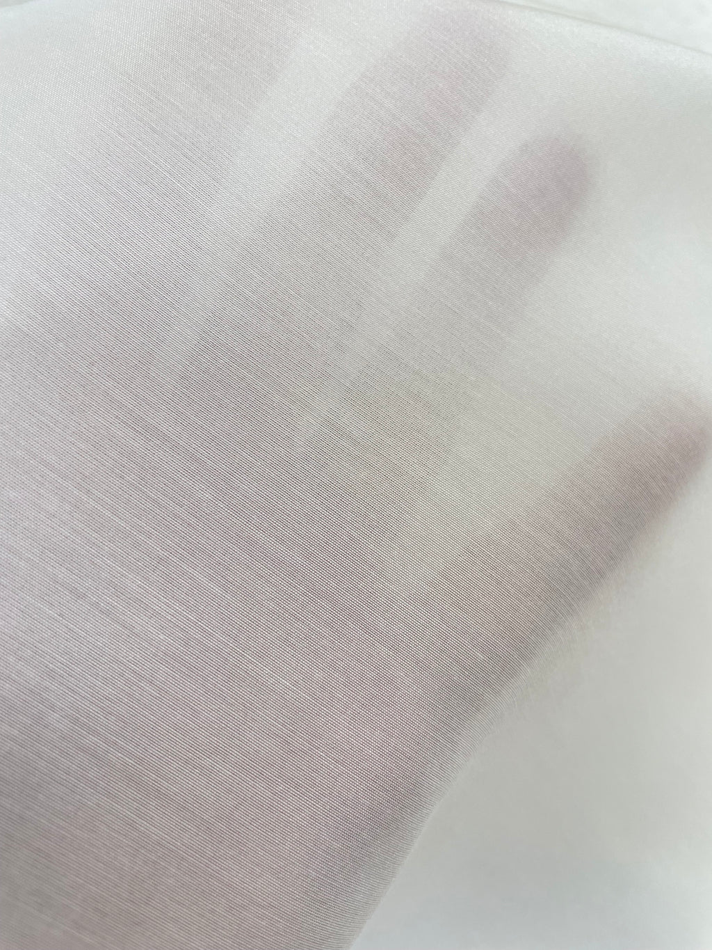 A close-up of a hand under an undyed white silk bamboo fabric, showing the texture and transparency of the material.
