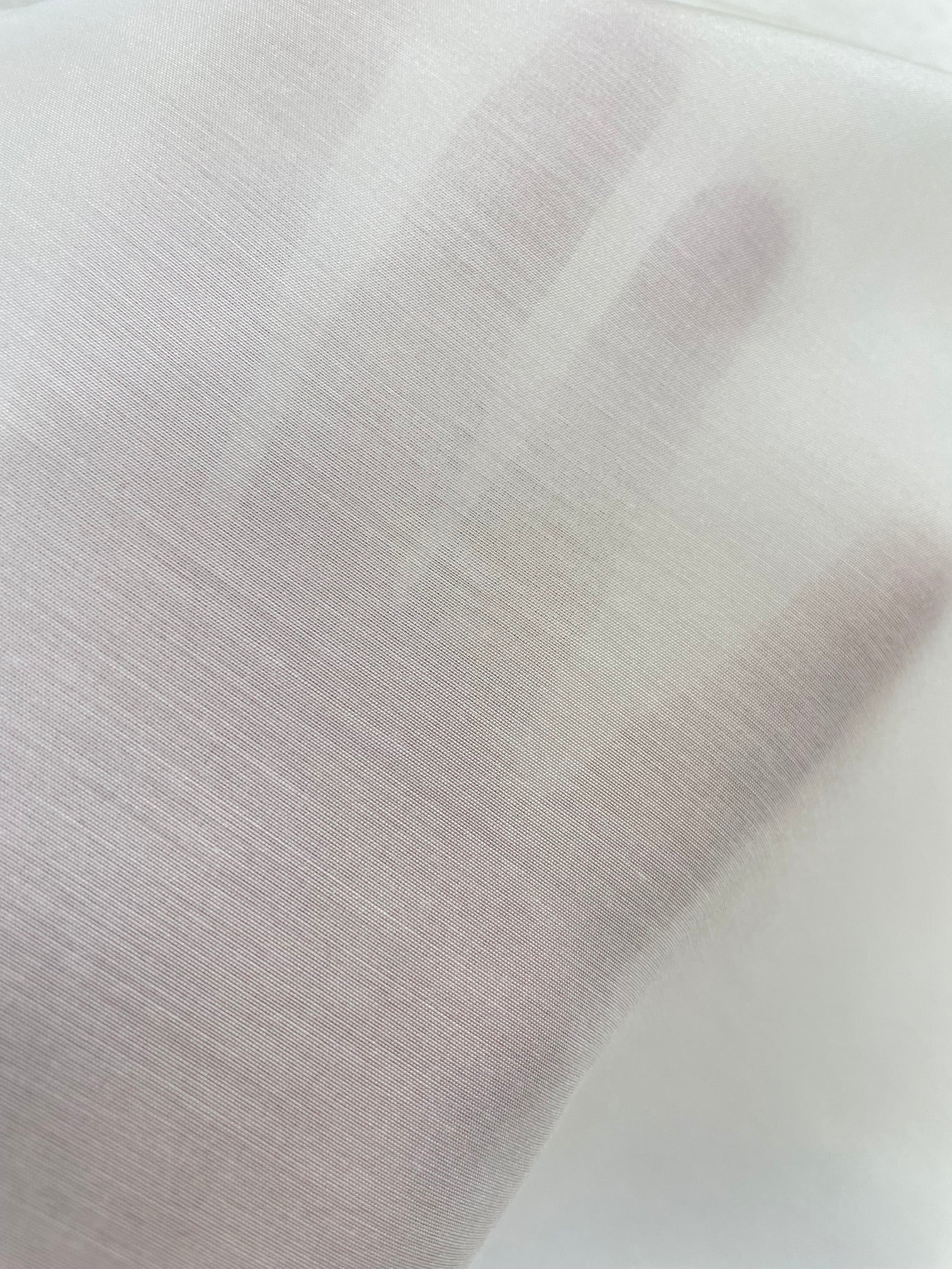 A close-up of a hand under an undyed white silk bamboo fabric, showing the texture and transparency of the material.