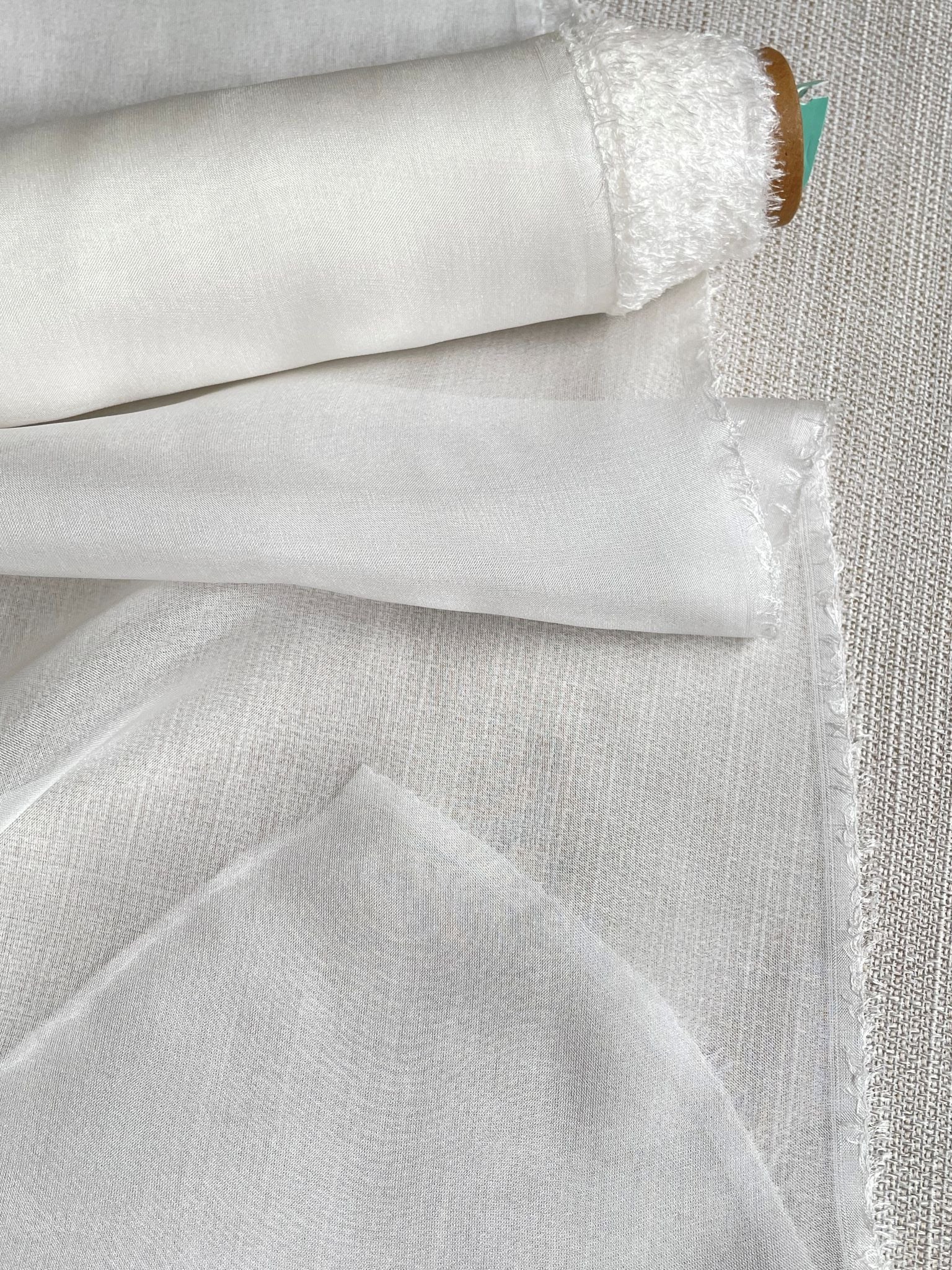 Close-up of undyed silk chiffon fabric with a textured pattern on a light gray background