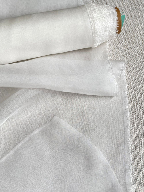 Close-up of undyed silk chiffon fabric with a textured pattern on a light gray background