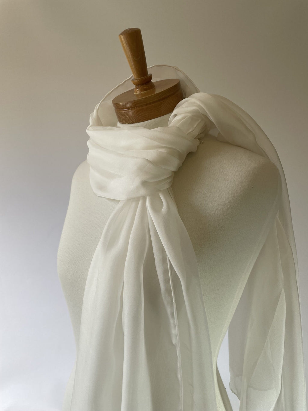 Undyed white silk chiffon scarf draped over a wooden mannequin on a plain background