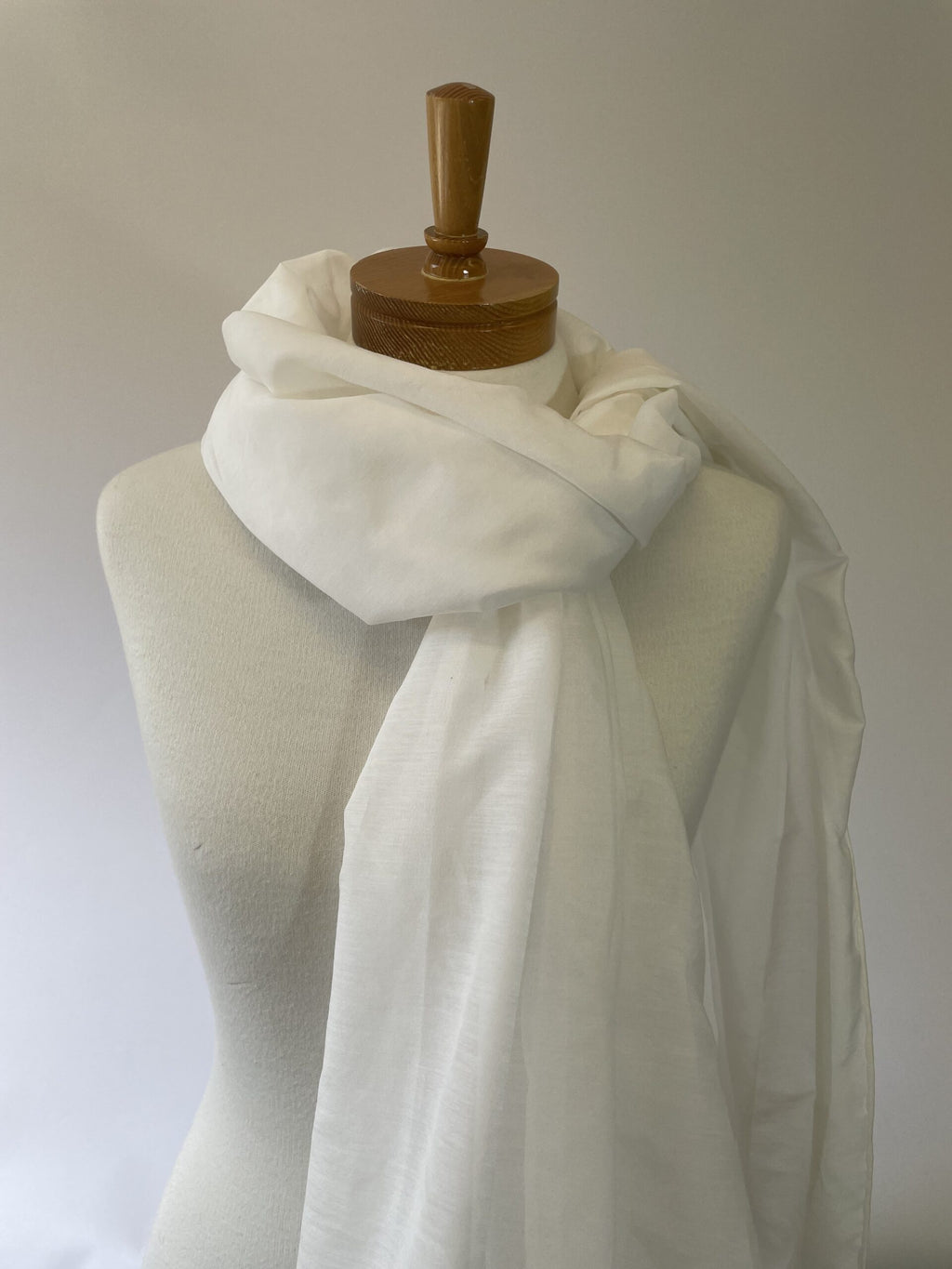 Undyed white silk cotton scarf draped over a mannequin with a wooden head on a plain background