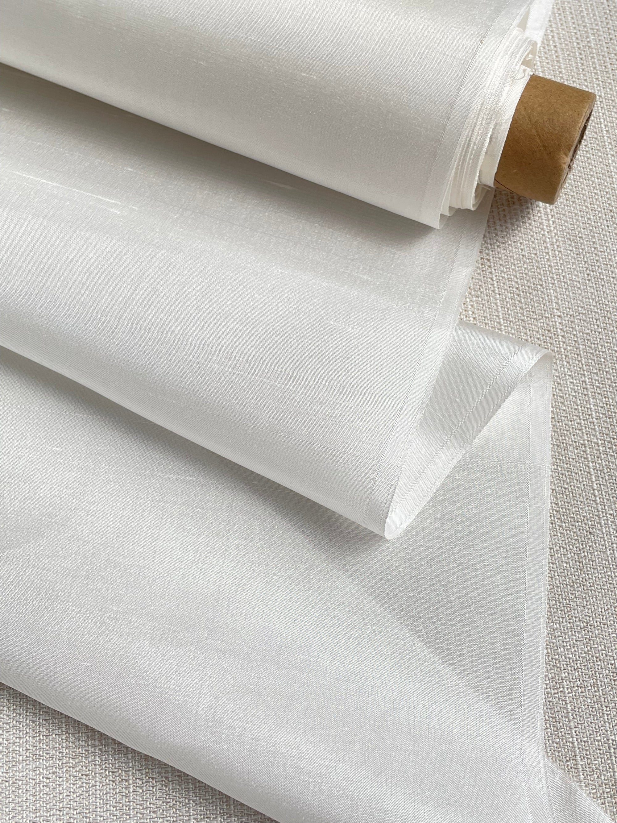 Roll of undyed silk dupioni fabric on a textured surface