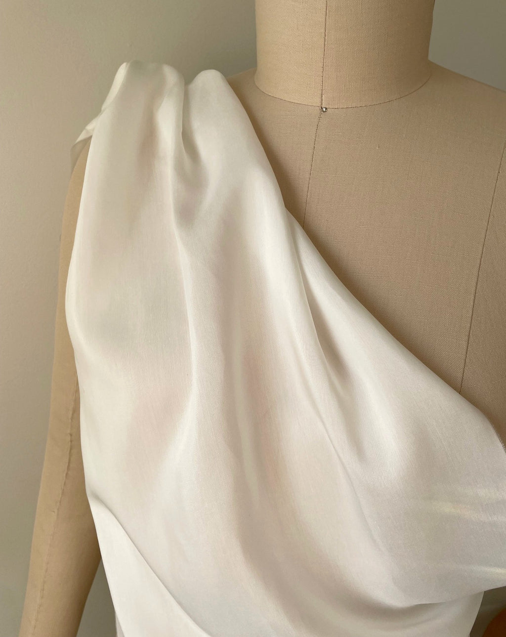 A draped off-white undyed silk bamboo fabric on a beige mannequin torso against a neutral beige background